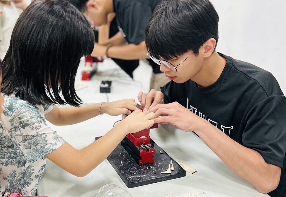 技優講師劉冠緯(右)指導南投孩童進行雷雕木工音樂盒。